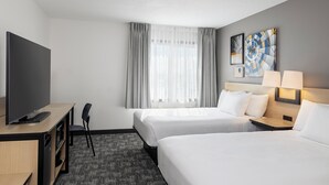 A hotel room with two beds, a desk with a TV, a chair, a desk lamp, and artwork on the wall. - City Express by Marriott Bemidji (Bemidji)