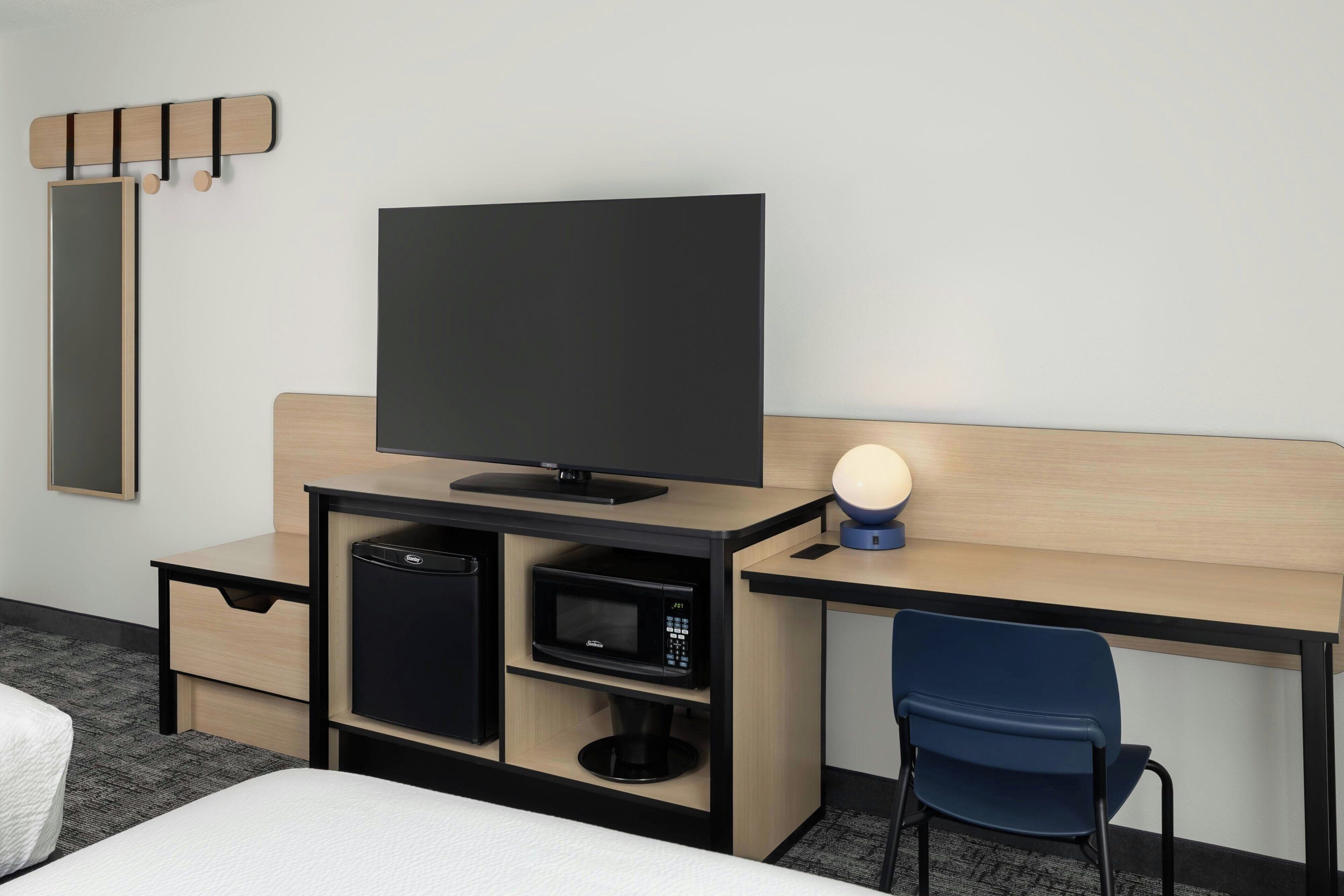Een hotelkamer met een bed, een bureau met een televisie, een magnetron, een kleine koelkast en een stoel.
