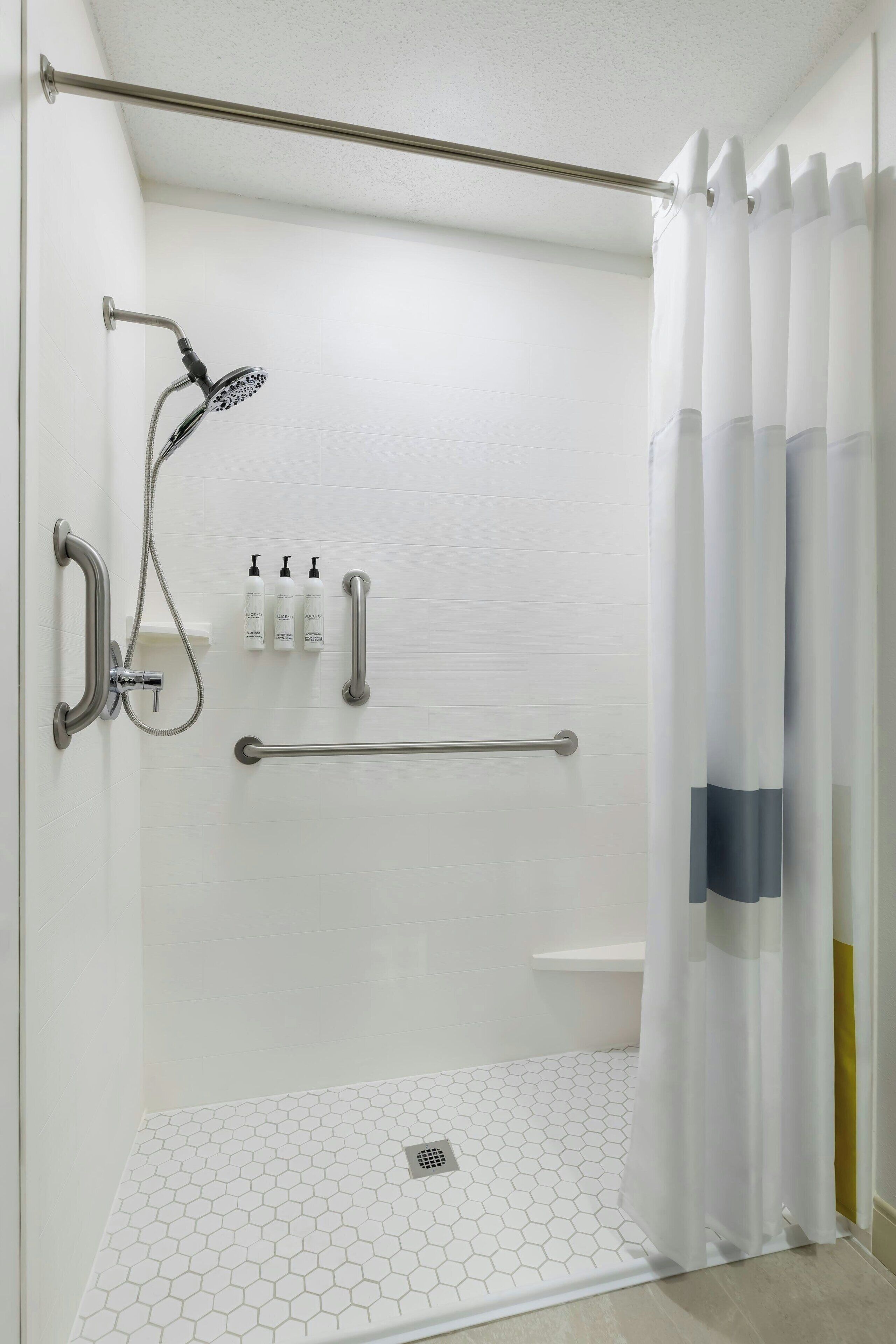 A shower area with a grab bar, a handheld showerhead, and a white tiled floor.
