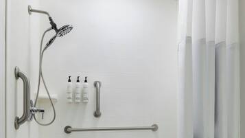 A shower area with a grab bar, a handheld showerhead, and a white tiled floor.
