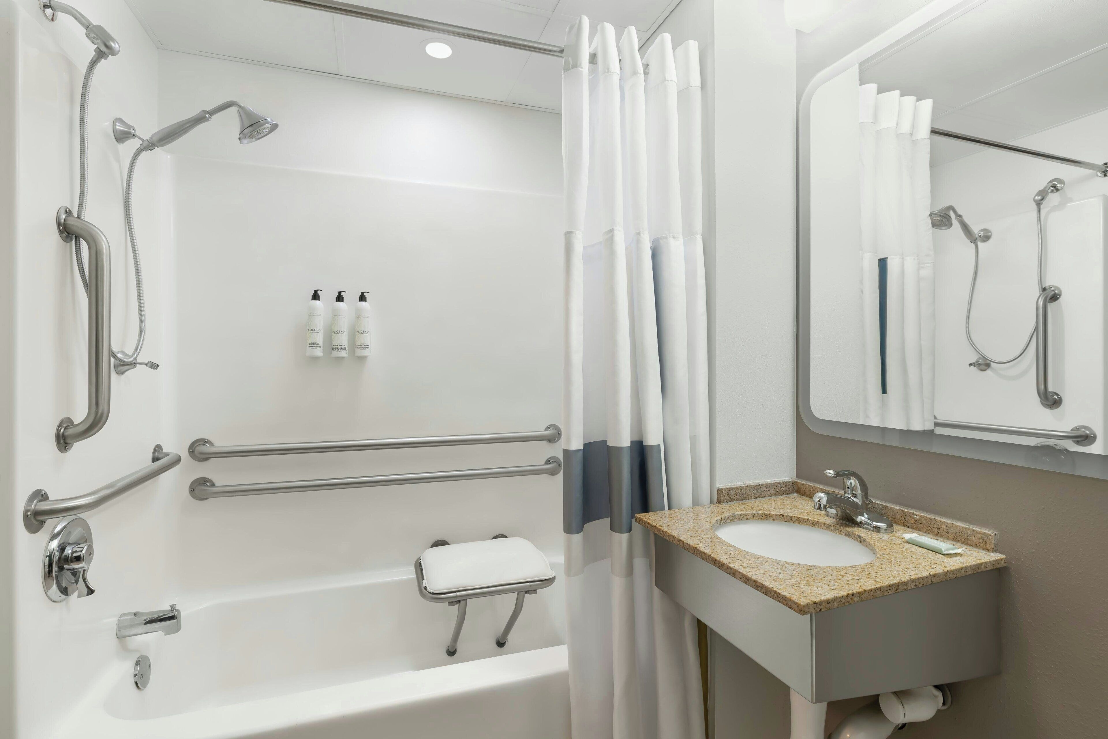 A bathroom with a bathtub, shower, grab bars, a white toilet, and a sink with a mirror.