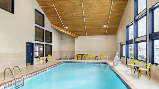 A swimming pool with a wooden ceiling, large windows, and yellow chairs. - City Express by Marriott Bemidji (Bemidji)
