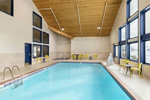 Una piscina con techo de madera, ventanas amplias y sillas amarillas.