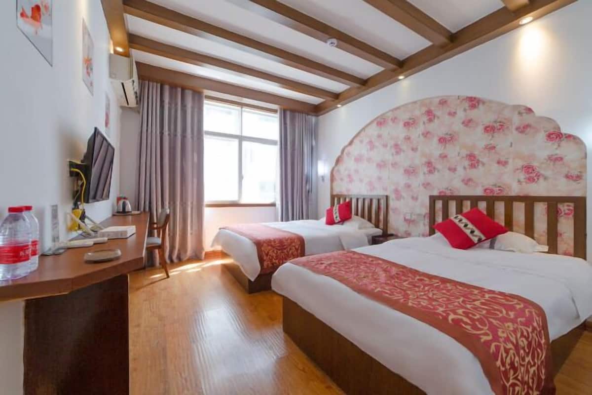 A hotel room with two beds, wooden beams on the ceiling, a desk with a computer, and a window with curtains.