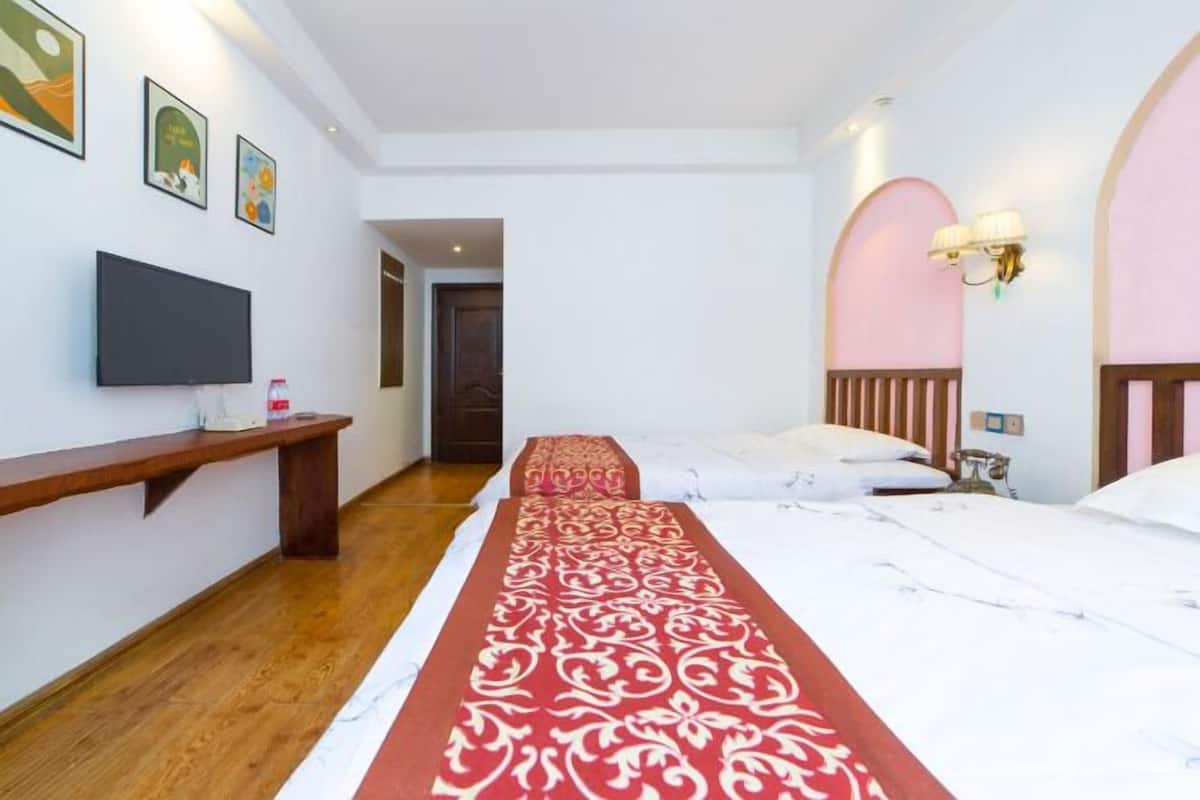 A hotel room with a bed, a TV, a wooden bench, and a hallway leading to another room.