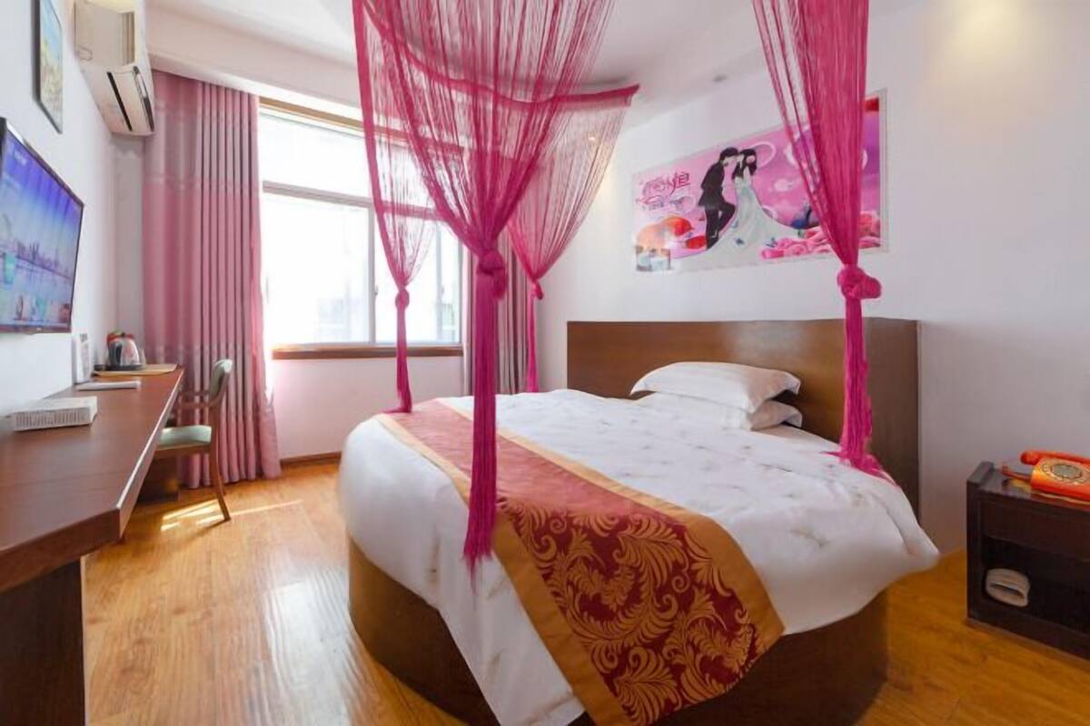 A hotel room with a bed, a desk, a chair, a TV, and a window with curtains.