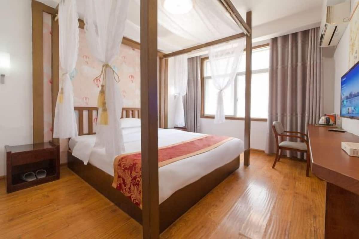 A bedroom with a four-poster bed, a wooden desk, a chair, and a television.