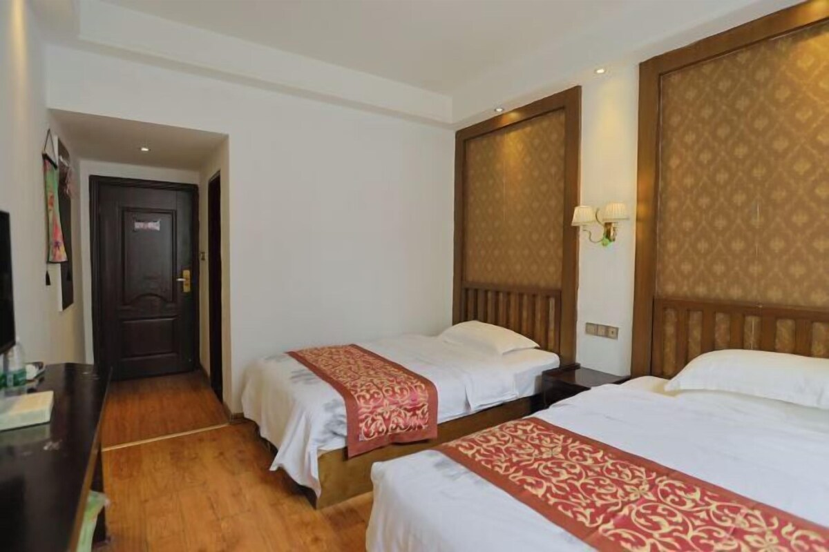 A hotel room with two beds, wooden headboards, a desk, and a door.