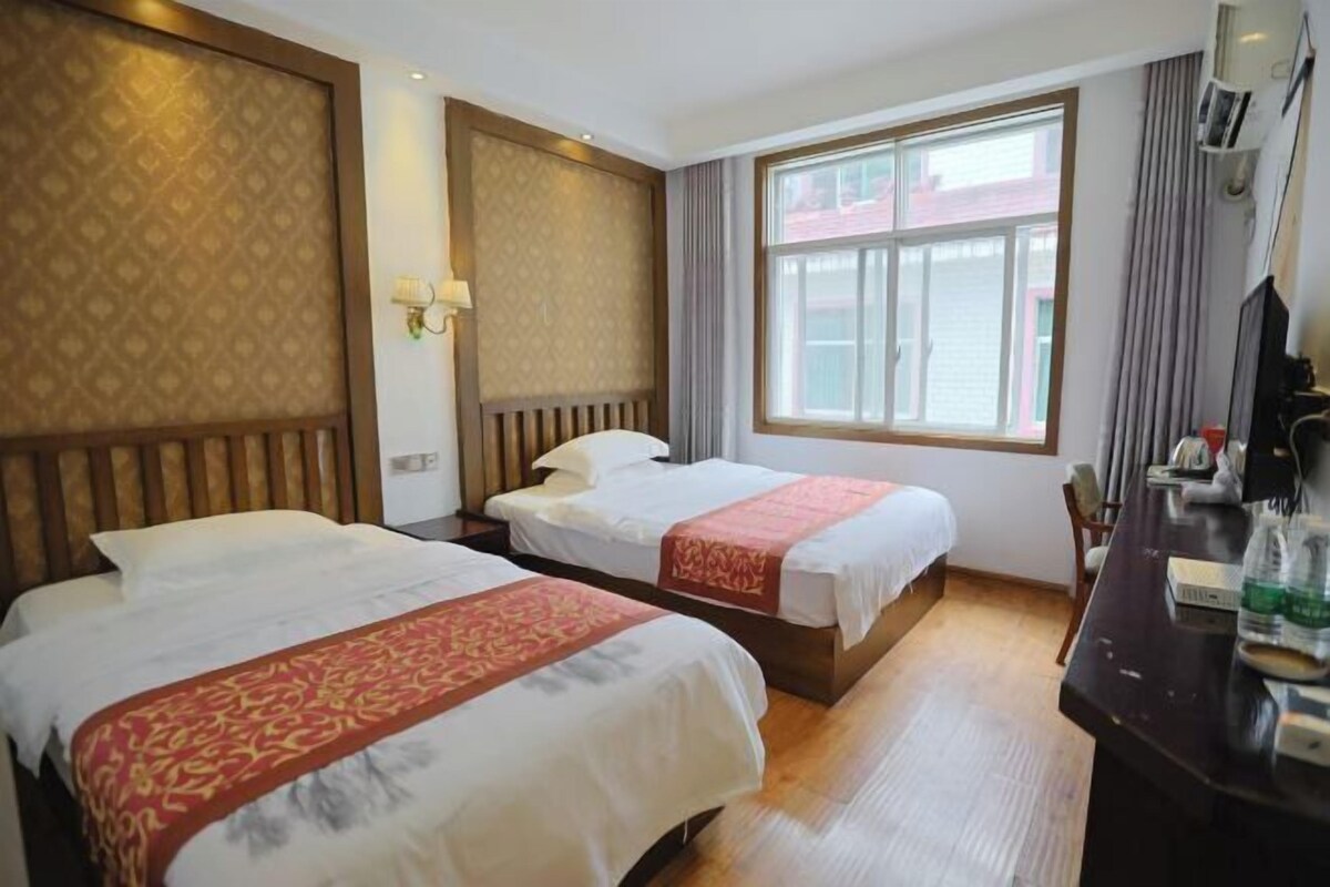 A hotel room with two beds, a large window, a desk with a chair, and a television.
