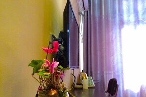 A room with a desk, a chair, a vase with flowers, a window with curtains, and a wall-mounted device. - Huatianju Inn (Zhangjiajie)
