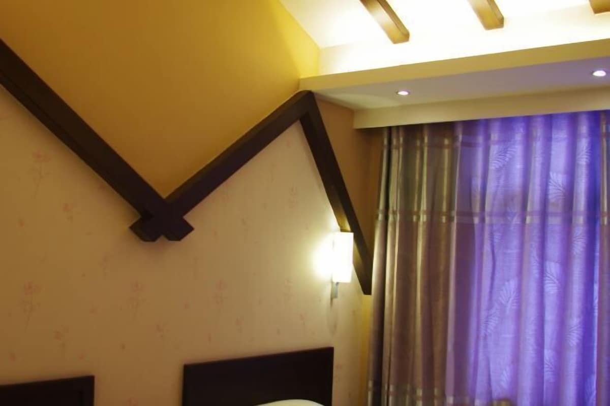 A hotel room with a bed, a headboard, a wall-mounted light, and a window with purple curtains.