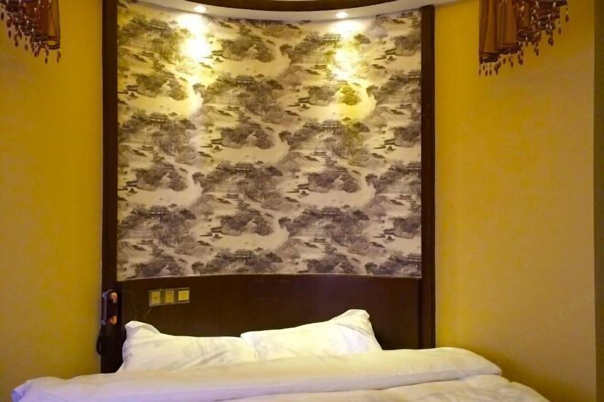 A hotel room with a bed, a wall with a traditional patterned wallpaper, and a wooden headboard.