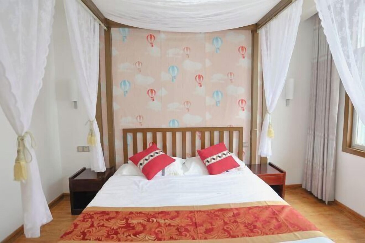 A bedroom with a bed, white curtains, a patterned wall, and a window.