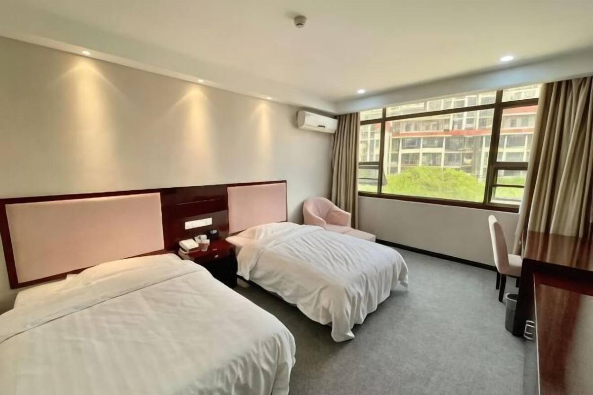 Hotellihuone, jossa on kaksi sänkyä, työpöytä, tuoli ja ikkuna, josta on näkymä vehreään maisemaan.