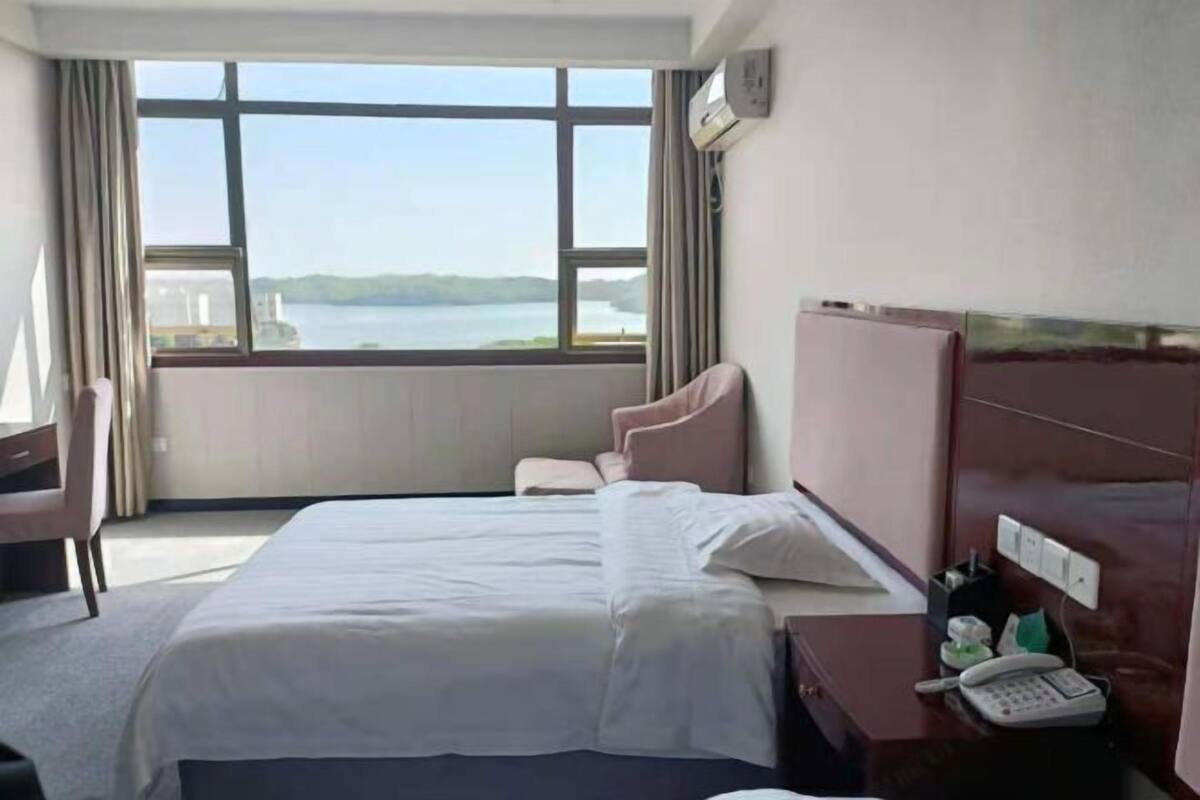Hotellihuone, jossa on suuri ikkuna, sänky, työpöytä ja puhelin.