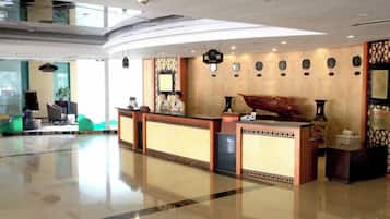 A hotel reception area with a reception desk, seating area, and a large window.