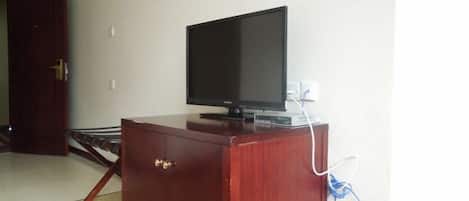 Un mueble de madera con un televisor encima, un enchufe y una puerta al fondo.
