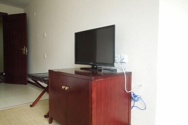 A wooden cabinet with a television on top, a power outlet, and a door in the background. - Sanhu Holiday Hotel (Jiayu)