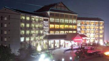 A multi-story hotel with a central atrium, large windows, and a parking area.