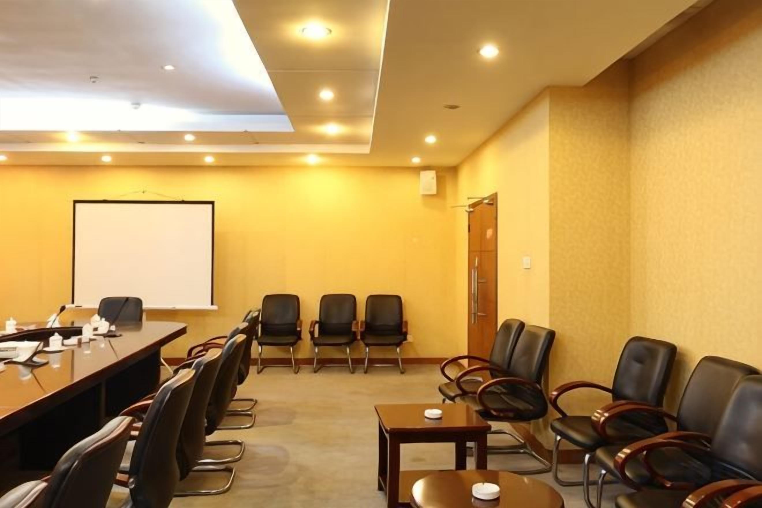 Un salón de conferencias con una larga mesa, varias sillas, una pizarra y una pantalla para proyector.