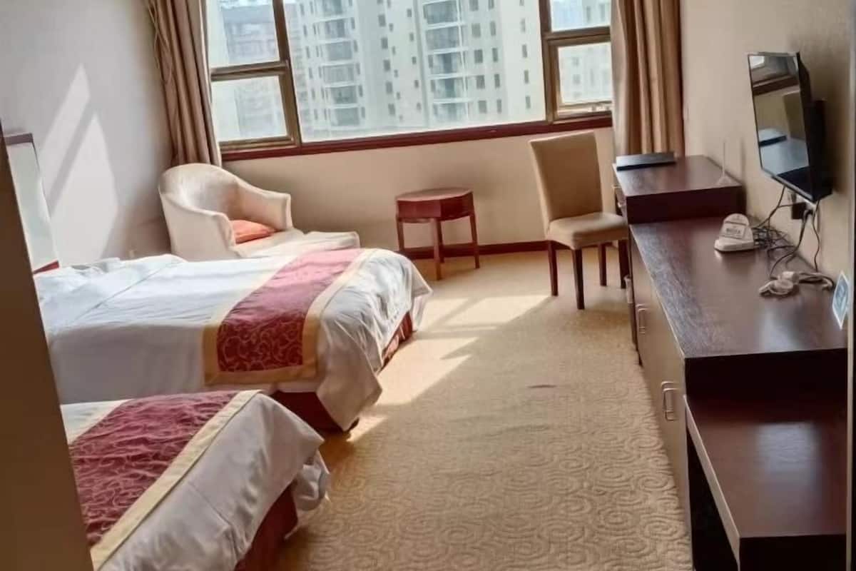 Two single beds with white bedding and red accents, a desk and chair, and a flat-screen TV.