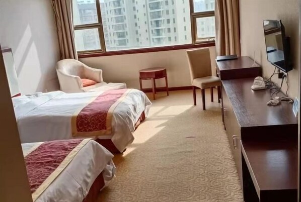 Habitación de hotel con dos camas, un escritorio, una silla, un televisor y una ventana con vistas a edificios.