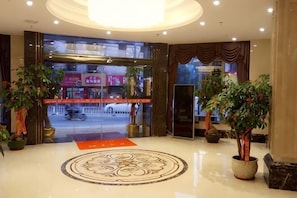 A hotel lobby with a large circular floor design, potted plants, and a view of the street outside.