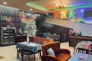 A restaurant interior with tables and chairs, a reception desk, and a neon sign. - Huaxia Hotel (Anxi)