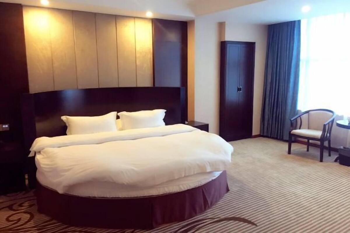 A hotel room with a large bed, a dark headboard, a chair, and a window with curtains.