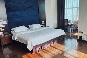 A hotel room with a bed, wooden flooring, a nightstand, a chair, and a window with curtains. - Huaxia Hotel (Anxi)