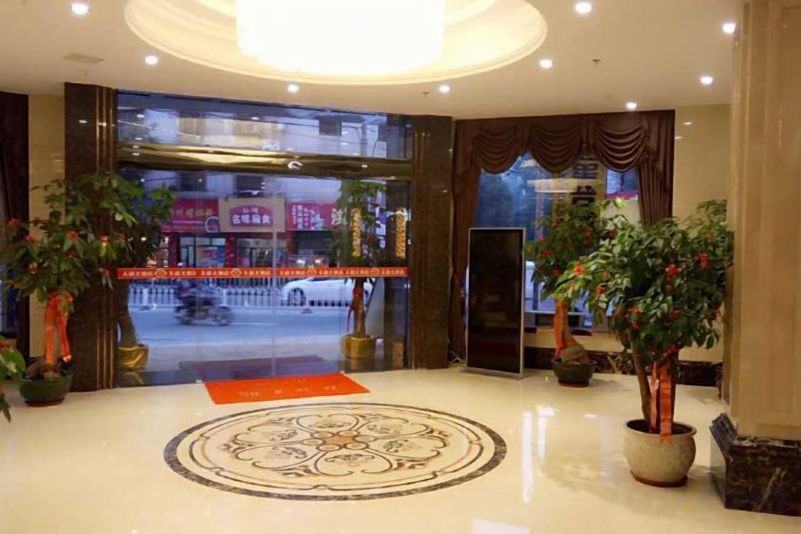 Un hall d’hôtel doté d’un grand sol circulaire orné de motifs, de plantes en pot et offrant une vue sur la rue.