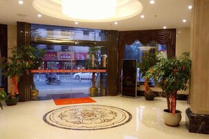 A hotel lobby with a large circular patterned floor, potted plants, and a view of the street outside.