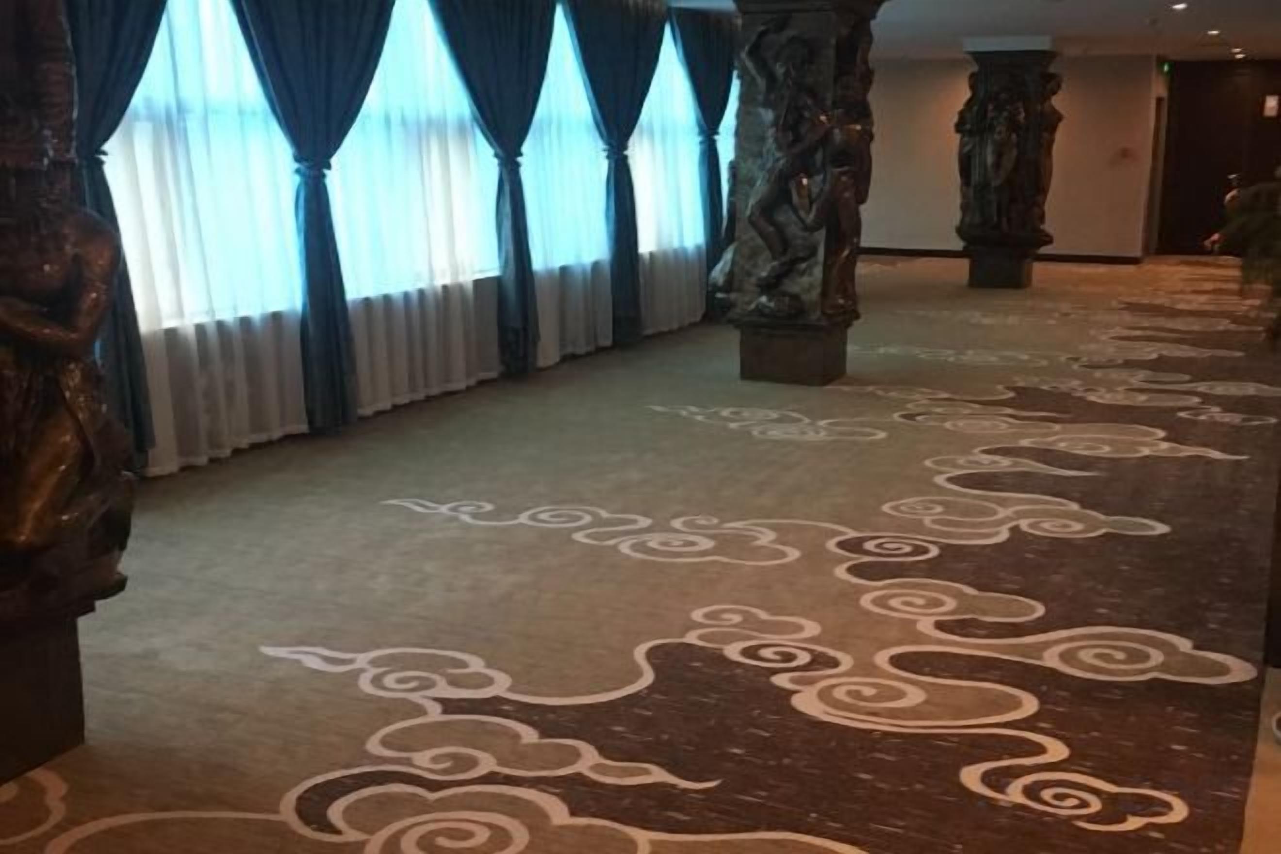 A corridor with patterned carpet, columns, and curtains.