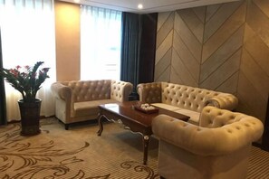 Una habitación de hotel con un sofá color beige, una mesa de centro de madera y una planta en maceta.