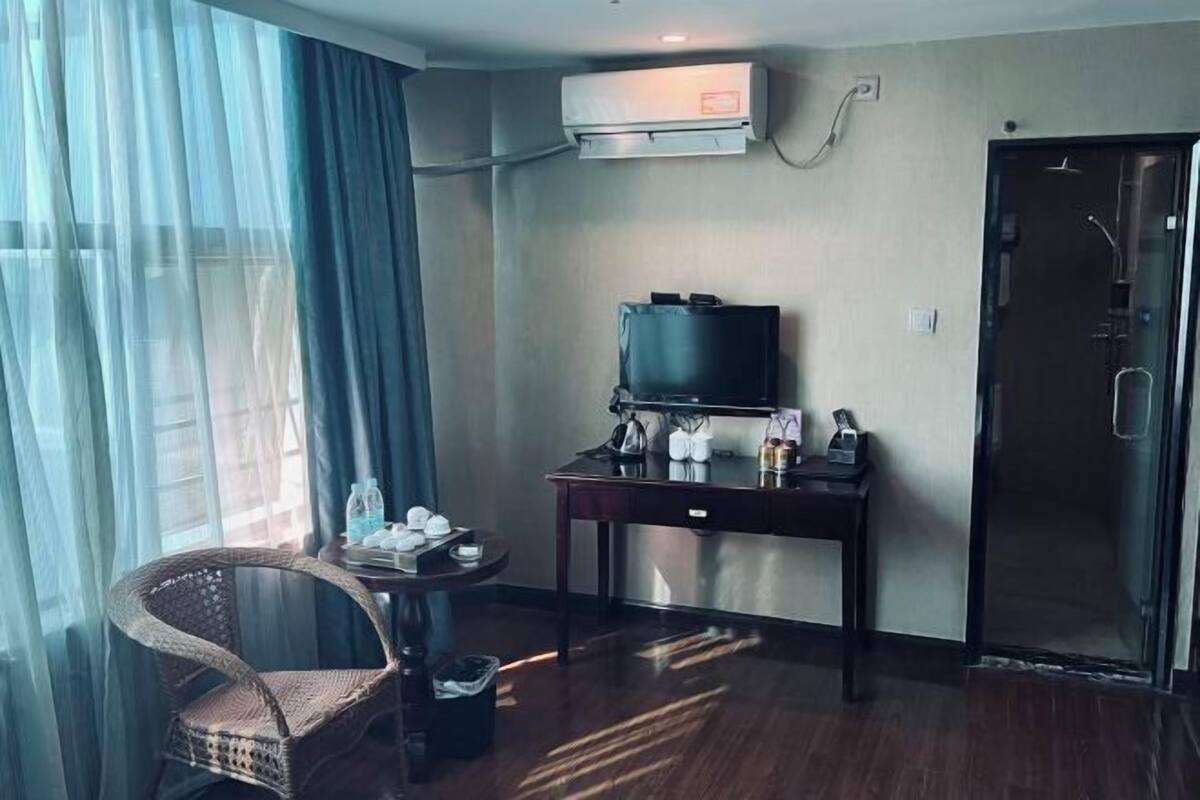 A hotel room with a television on a desk, a chair, a trash bin, and a door.
