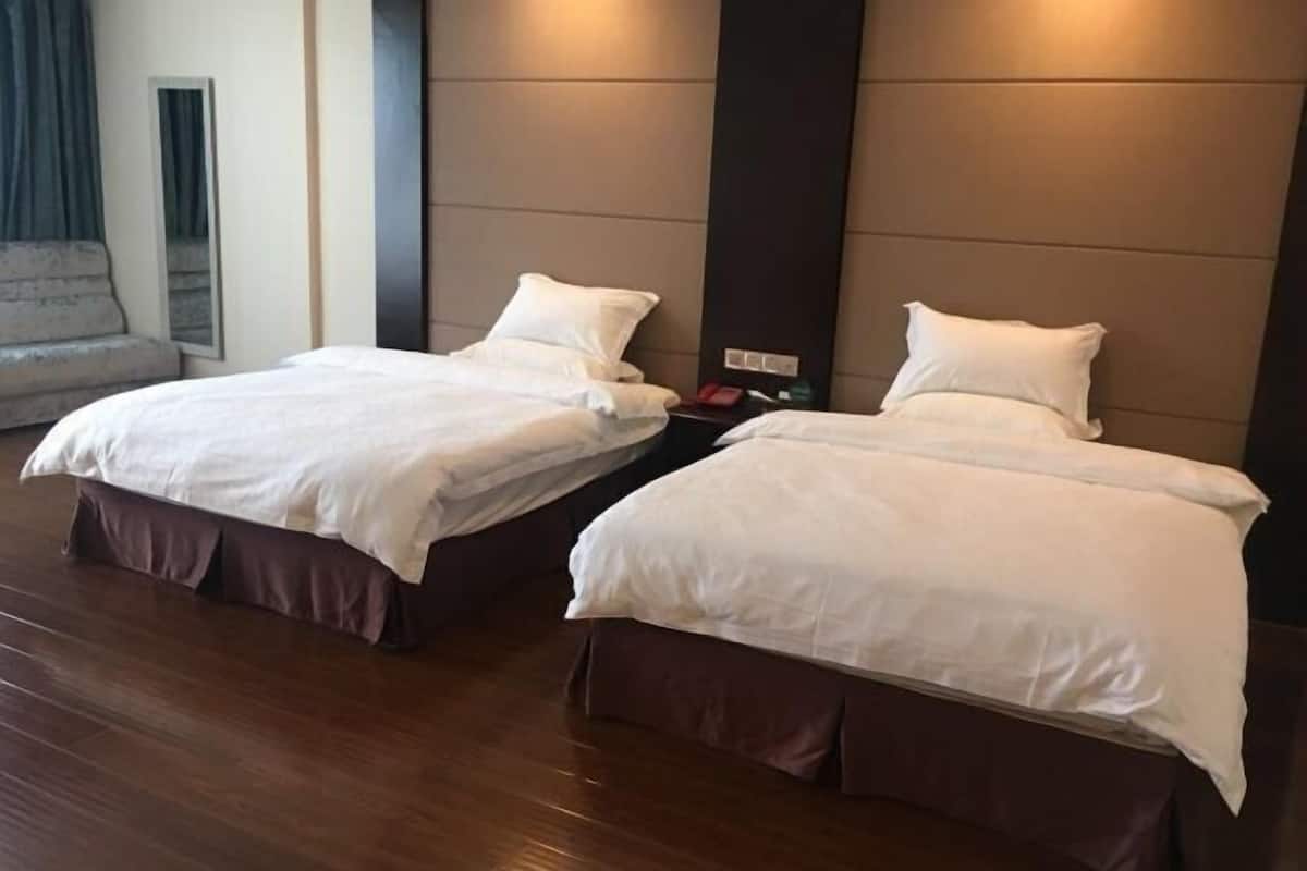 Two beds with white bedding in a room with wooden flooring and a dark headboard.