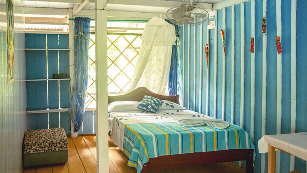 Ein Zimmer mit einem Bett, einer Bank, einem Tisch und einem Ventilator.