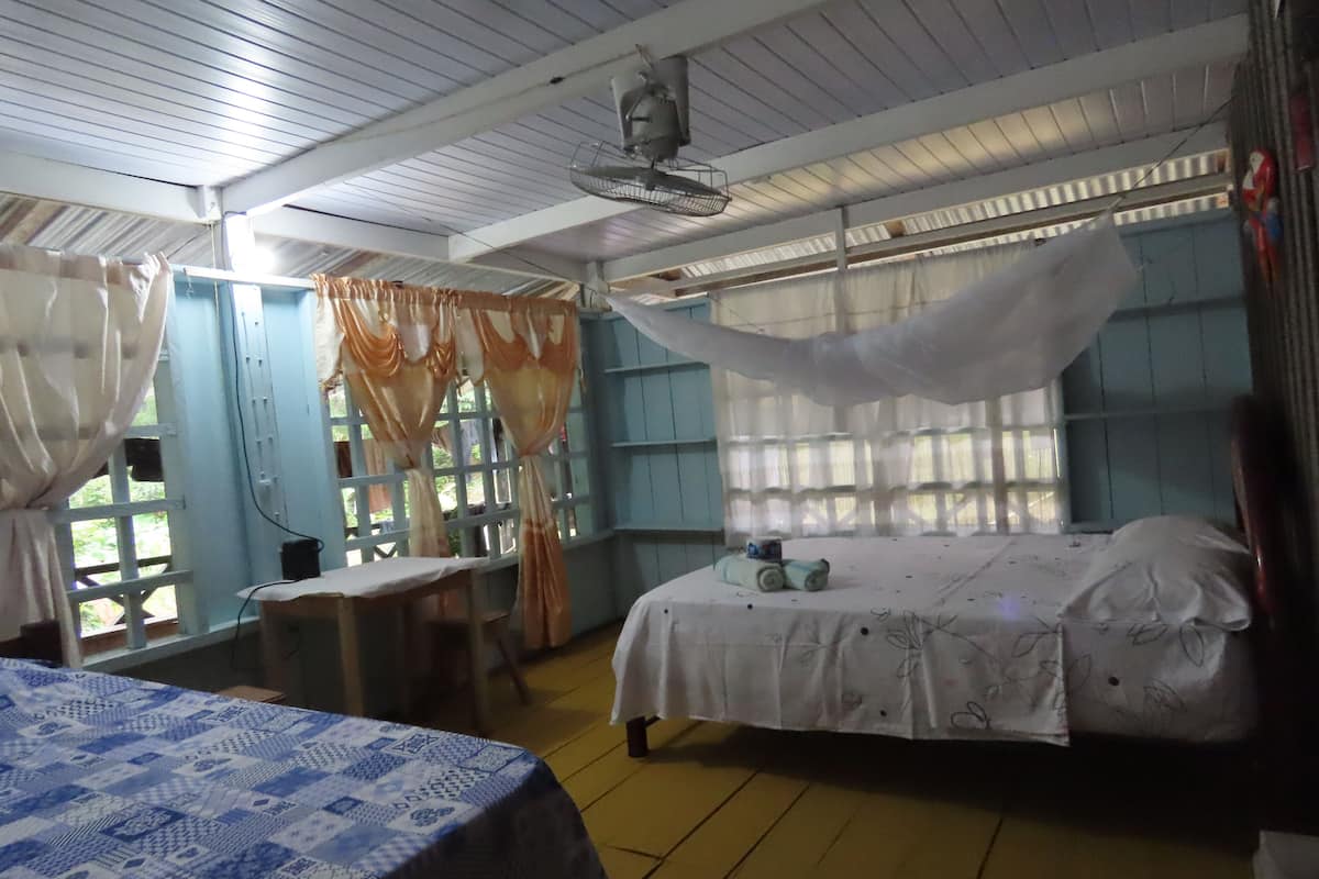 Une pièce comprenant un lit, un bureau et une chaise. Il y a une fenêtre avec des rideaux et un ventilateur au plafond.