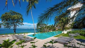 A pool area with lounge chairs, a clear blue sky, and a view of the ocean. - Sayan Tropical 43 New Luxury Oceanfront Condo (Puerto Vallarta)