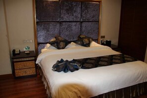 A neatly made bed with a headboard, a bedside table with a lamp, and a wall socket. - Xiangqu Garden Hotel (Shannan)