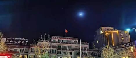 Un hotel de varios pisos con una bandera en la cima, ventanas iluminadas y un cielo nocturno despejado.