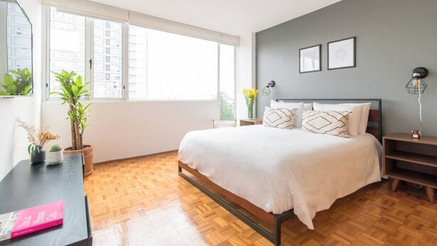 Een moderne slaapkamer met een groot bed, houten vloeren, een bureau met een boek en potplanten.