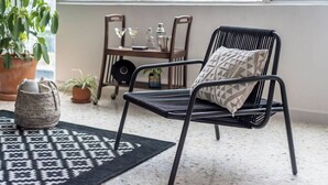 Een moderne woonkamer met een zwarte metalen stoel, een getextureerd vloerkleed en een stadszicht door een groot raam.