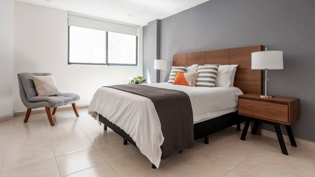 Une chambre moderne avec un grand lit, des lampes de chevet, un fauteuil et une fenêtre.
