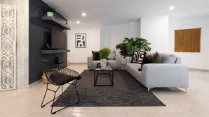 Un salon moderne avec un canapé gris, un fauteuil noir, une table basse et un téléviseur posé sur un meuble noir. On y trouve également deux plantes en pot et un tableau encadré accroché au mur.