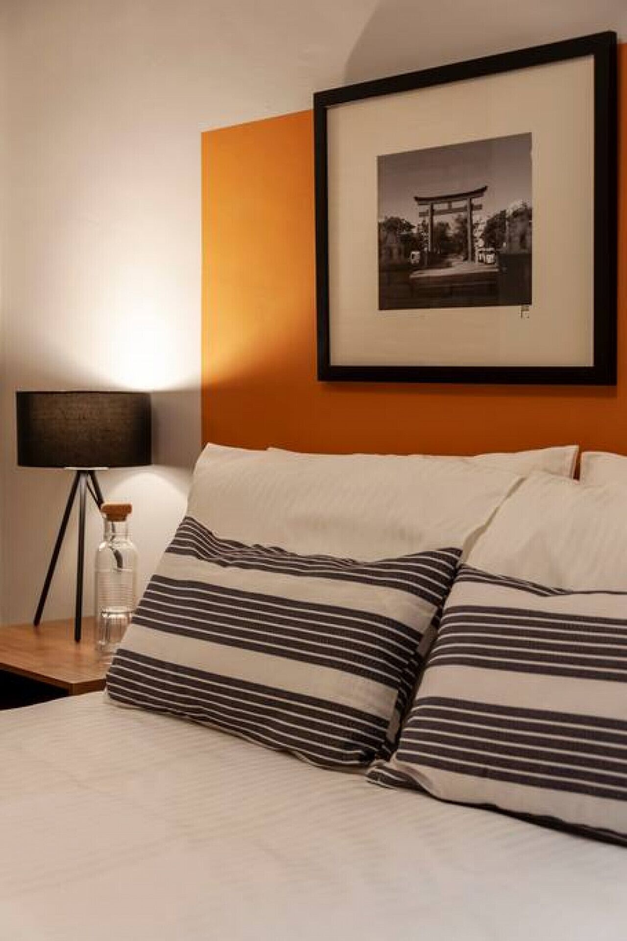 A neatly made bed with striped pillows, a framed picture on the wall, and a bedside lamp.