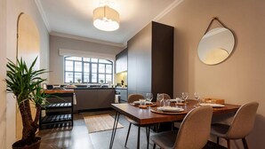 A modern dining area with a large table set for four, a kitchen in the background, and a potted plant on the left. - Newly-Renovated Studio in a 1920's Modern House (Ciudad de México)