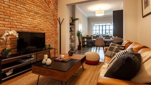 A living room with a brick wall, a flat-screen TV, a coffee table, a sofa, and a dining area in the background. - Newly-Renovated Studio in a 1920's Modern House (Ciudad de México)