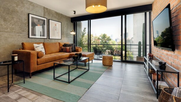 Un salon moderne avec un canapé, une table basse et un téléviseur fixé au mur, qui est en briques.