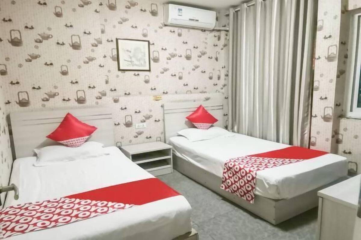 Een hotelkamer met twee bedden, elk voorzien van een rood kussen, een klein tafeltje en een raam met gordijnen.